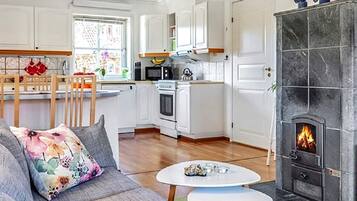 A modern kitchen with white cabinets, a dining area with a wooden table, and a fireplace with a visible fire.