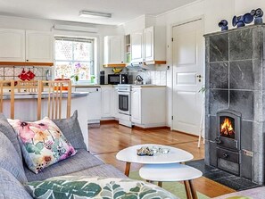 A modern kitchen with white cabinets, a dining area with a wooden table, and a fireplace with a visible fire.