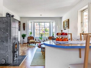 A modern living room with a fireplace, a dining area with a fruit display, and large windows offering a view of the outdoors. - 4 Person Holiday Home in Motala (Motala)