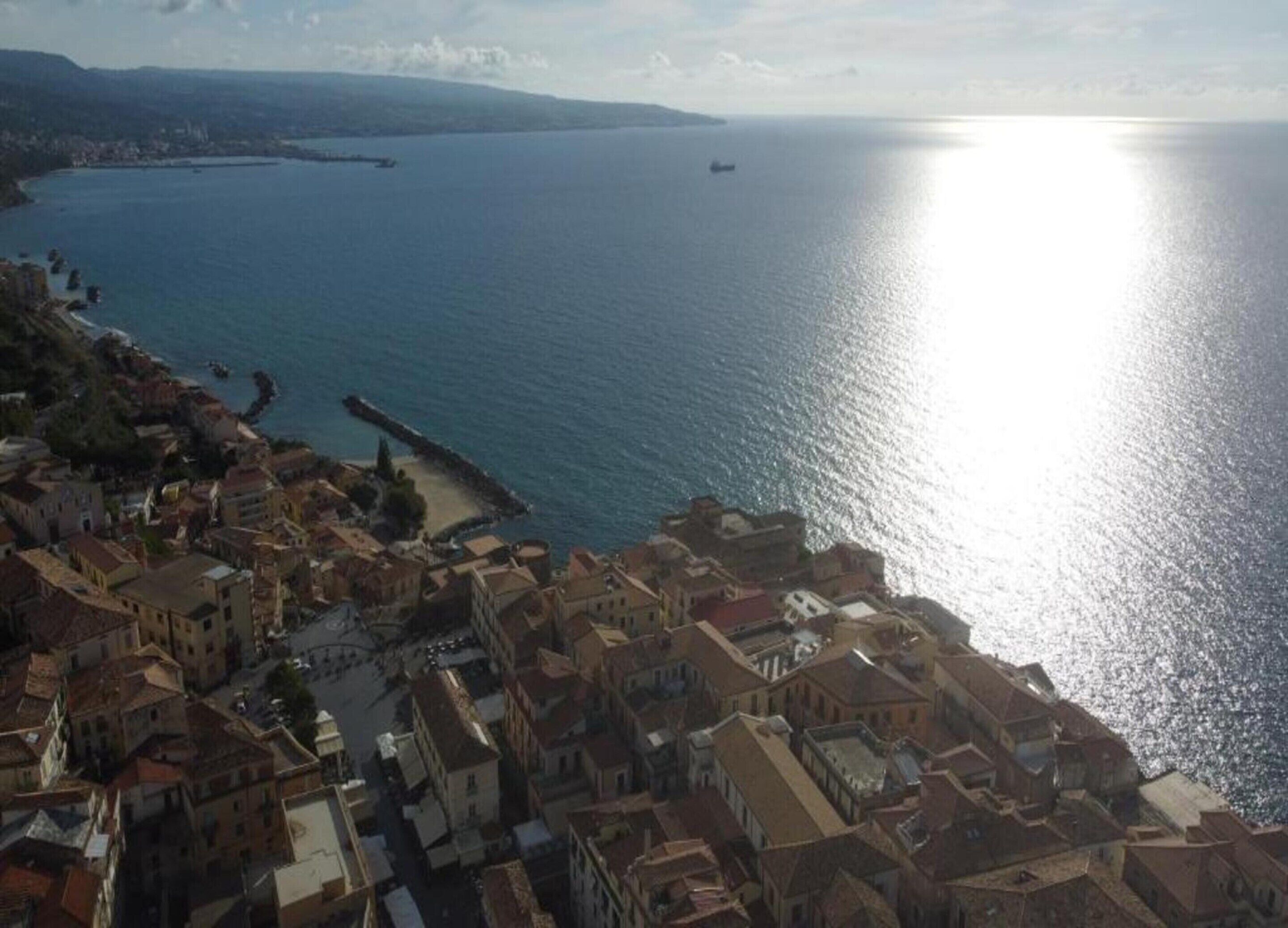 A coastal town with buildings along the waterfront, a clear view of the sea, and a distant ship.