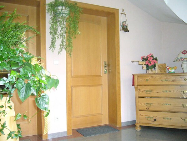 Een houten deur met een hangplant, een houten dressoir met lades, en een kleine lamp op het dressoir.