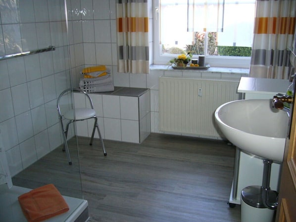 Un baño con ducha, inodoro, lavamanos y ventana con cortinas.