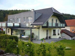 Een moderne twee-onder-een-kapwoning met een balkon, een overdekte patio en een verzorgde tuin.