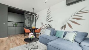 Ein modernes Wohnzimmer mit einem grauen Sofa, einem runden Couchtisch und einer Küchenzeile im Hintergrund.