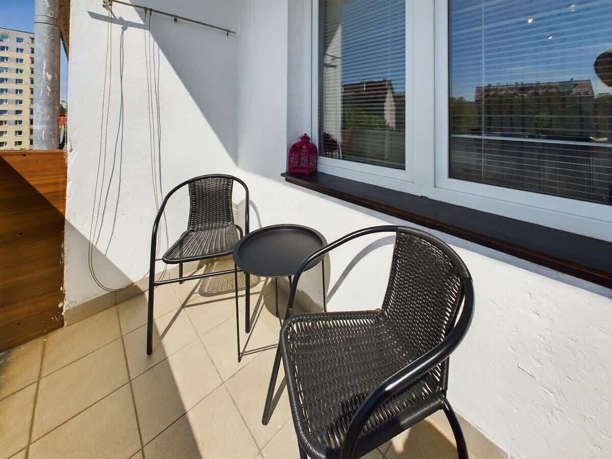 Een balkon met twee zwarte rieten stoelen en een kleine ronde tafel.