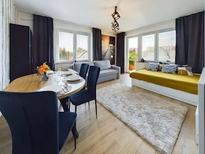 A modern living room with a dining area, large windows, a sofa, and a yellow bench.