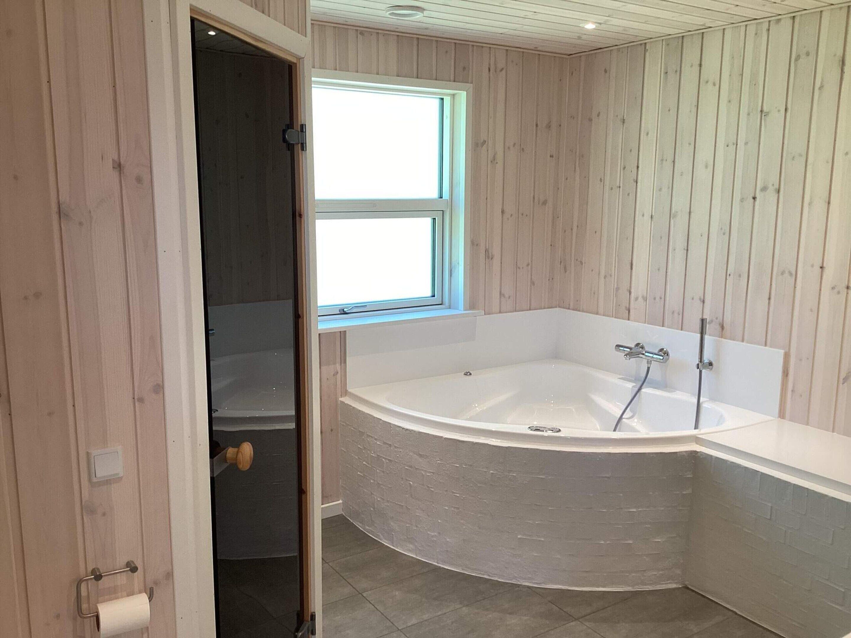 Une salle de bain avec une baignoire sur pieds, une fenêtre et un lambris en bois.
