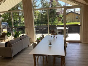 A spacious room with a large dining table, a sofa, and a view of the outdoors through large windows.