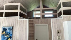 A room with wooden walls and a sloped ceiling, featuring a bunk bed, a door, and a window. - 8 Person Holiday Home in Hals (Hals)