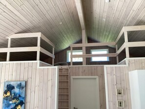 Una stanza con pareti in legno e soffitto spiovente, con un letto a castello, una porta e una finestra.