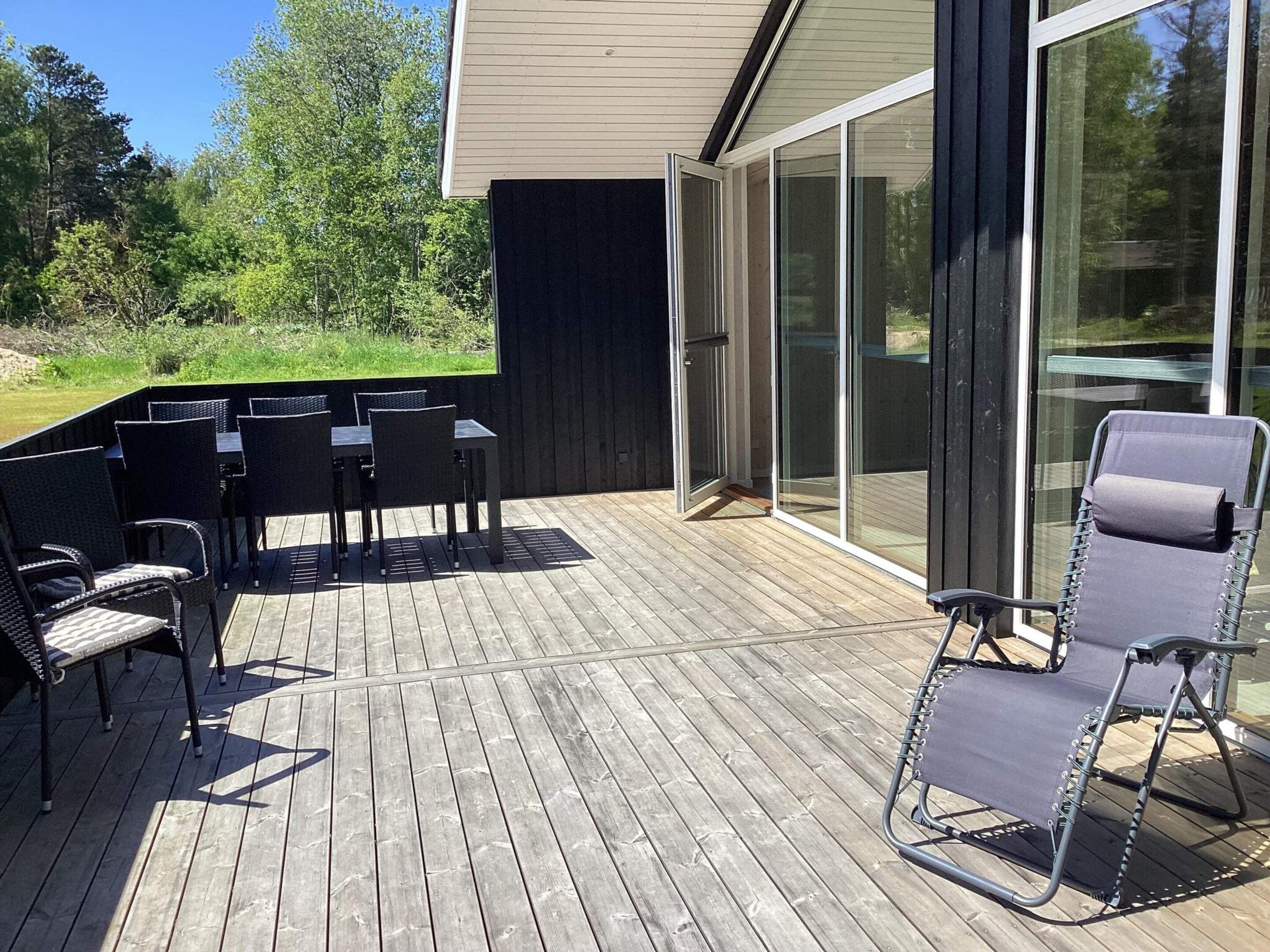 An outdoor deck with a table and chairs, a lounge chair, and a sliding glass door leading to a covered area.