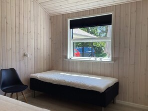 A small room with a single bed, a chair, and a window with a view of parked cars outside.