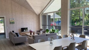 A modern living room with a sofa set, a dining table with chairs, a television, and a large window with a view of the outdoors. - 8 Person Holiday Home in Hals (Hals)