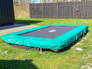 A trampoline with a green safety pad, set on a grassy lawn.
