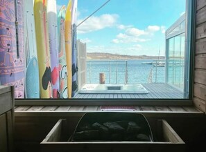 Una habitación con vista al mar, un jacuzzi y tablas de surf apoyadas en la pared.