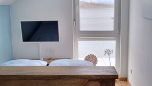 Un dormitorio con una cama de madera, un televisor en la pared y una ventana con vista a una masa de agua.