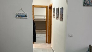 Um corredor com uma cama de beliche ao fundo, uma placa de boas-vindas e algumas fotos emolduradas na parede.