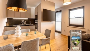 A modern kitchen with a black pendant light, a dining area with a wooden table and grey chairs, and a guest card on the wall. - Apartment With Shared Infinity Pool (Sankt Martin am Tennengebirge)