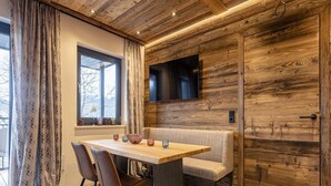 A modern dining area with a wooden table, chairs, and a bench. A flat-screen TV is mounted on the wall. - Apartment With Shared Infinity Pool (Sankt Martin am Tennengebirge)