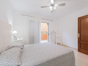 A bedroom with a bed, a ceiling fan, a nightstand, a lamp, a chair, and a door. - Belvilla by OYO Casa A-a3 Corralejo (La Oliva)