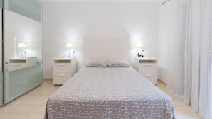 A bedroom with a bed, two bedside tables with lamps, a ceiling fan, and a large window with sheer curtains. - Belvilla by OYO Casa A-a3 Corralejo (La Oliva)