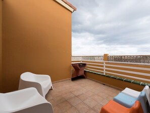A balcony with a tiled floor, white plastic chairs, a barbecue grill, and a white fence. - Belvilla by OYO Casa A-a3 Corralejo (La Oliva)