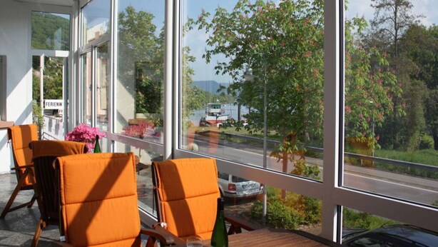 A dining area with orange chairs and a table, large windows with a view of a road and greenery. - Appealing Apartment in Alf (Alf)