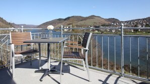 A balcony with a table and two chairs, overlooking a body of water and a hilly landscape. - Appealing Apartment in Alf (Alf)