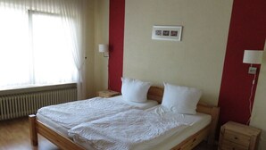 A bedroom with a wooden bed, white bedding, a red accent wall, and a window with curtains. - Appealing Apartment in Alf (Alf)