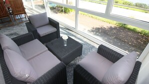A sunlit room with wicker furniture and a view of a road and greenery outside. - Appealing Apartment in Alf (Alf)