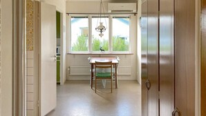Um corredor com uma mesa de jantar e cadeiras, uma janela com vista para o verde e uma porta fechada.