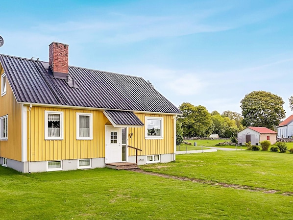 A yellow house with a black roof, a chimney, and a small porch.