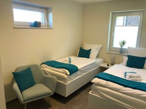 Een hotelkamer met twee eenpersoonsbedden, een stoel, een nachtkastje en een raam met uitzicht op een gebouw van baksteen.