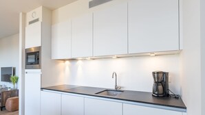 A modern kitchen with white cabinets, a stainless steel microwave, a coffee maker, and a built-in oven. - Apartment on the 2nd Floor for Family (Middelkerke)