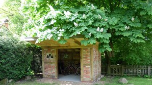 A small brick structure with a covered entrance, a bicycle parked inside, and a wooden fence in the background. - Holiday Home Hirtenkate Apartment 2 (Soderstorf)