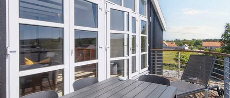 Une terrasse avec une table et des chaises, une porte vitrée donnant sur un espace intérieur et une vue sur les environs.