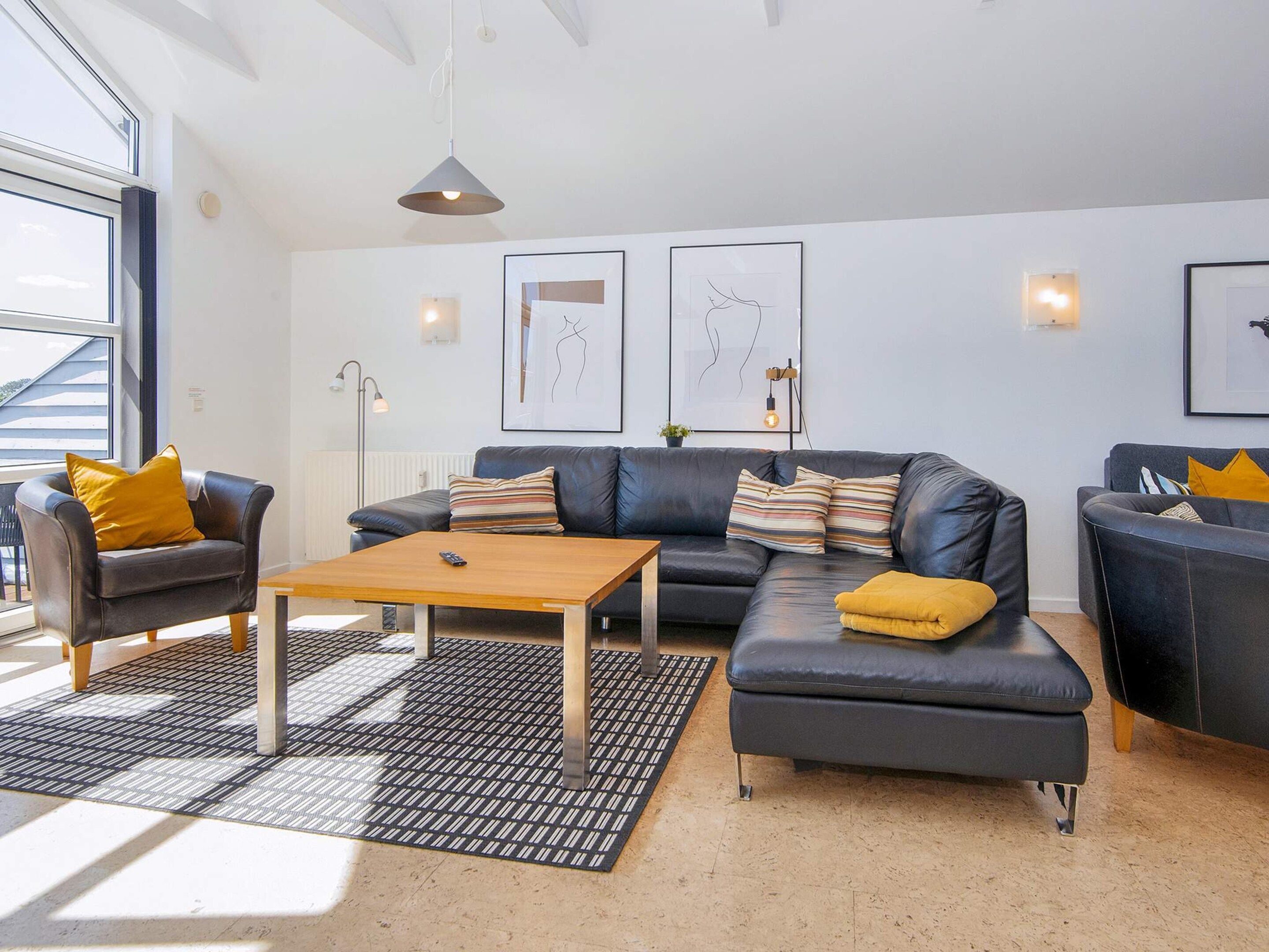 A modern living room with a sofa, armchair, and ottoman, a wooden coffee table, and a patterned rug.
