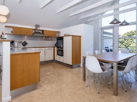 Una cocina moderna con una isla central, armarios blancos, electrodomésticos de acero inoxidable y un comedor con sillas blancas.