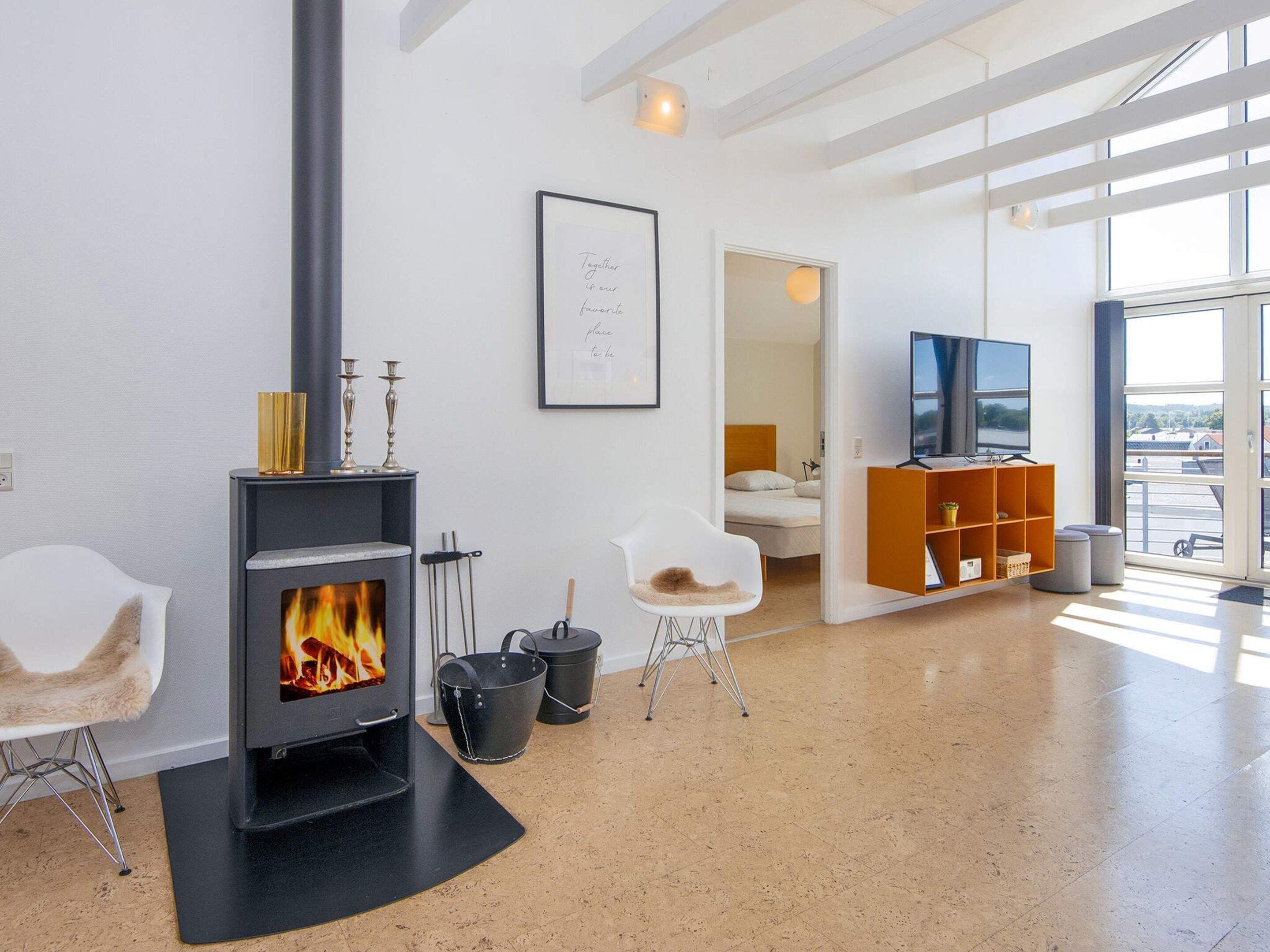 A modern living room with a fireplace, a framed quote on the wall, a TV, and a view through large windows.