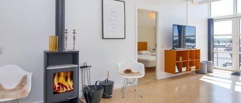 A modern living room with a fireplace, a framed quote on the wall, a TV, and a view through large windows.