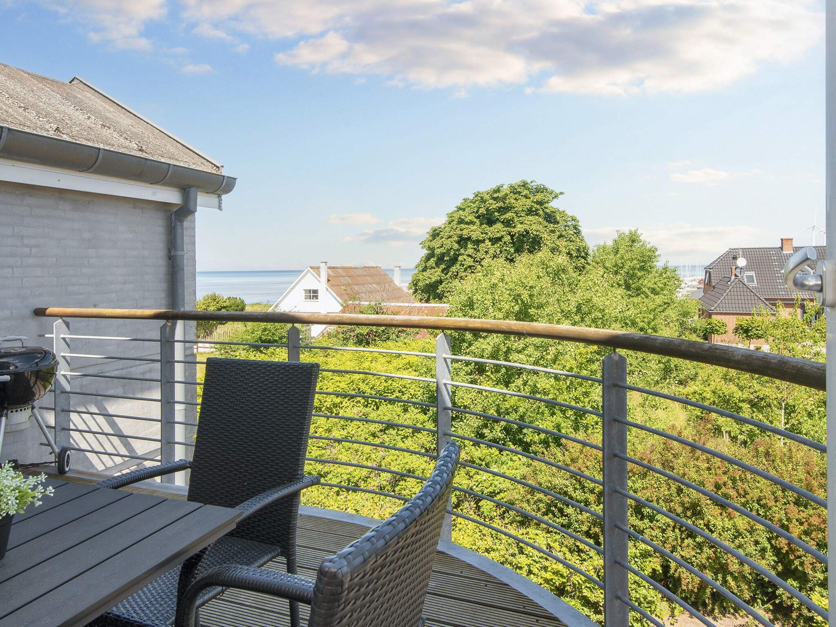 A balcony with a table and chairs, overlooking a residential area with houses and a tree.
