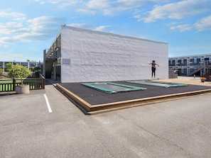 A trampoline area with a white wall backdrop, a small outdoor seating area, and a building with a balcony in the background. - 6 Person Holiday Park Home in Glesborg (Glesborg)