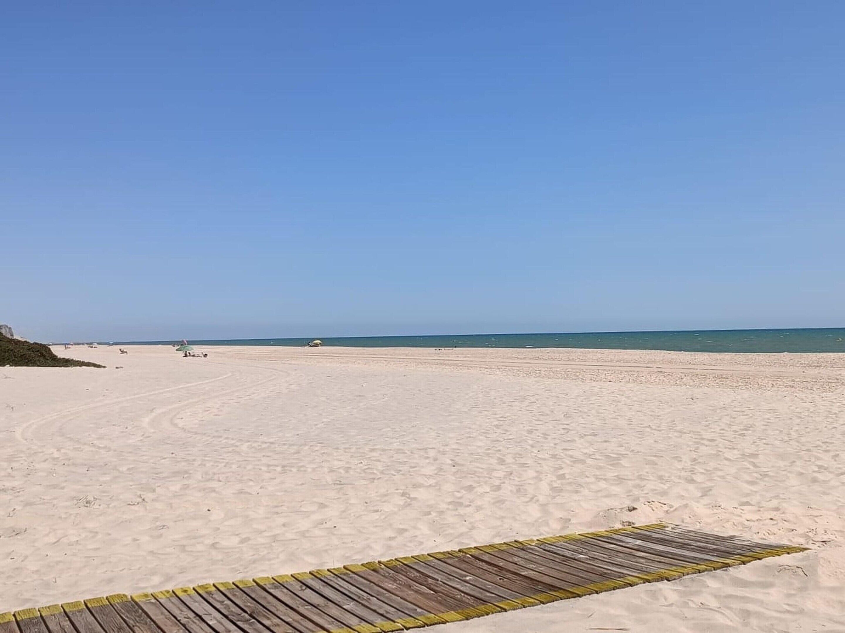 A wide sandy beach with a wooden boardwalk leading to the water.