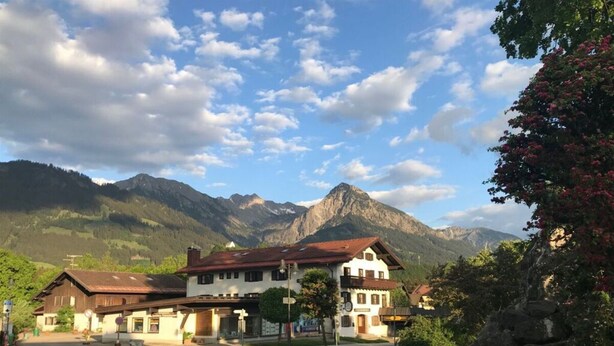 A traditional chalet-style building with a central entrance, surrounded by lush greenery and a mountain backdrop. - Pleasant Apartment in Fischen (Fischen im Allgaeu)