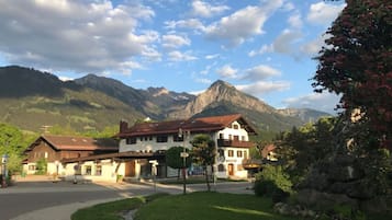 A traditional chalet-style building with a central entrance, surrounded by lush greenery and a mountain backdrop.
