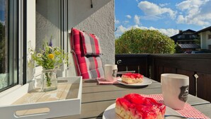 A dining table with a slice of cake and a mug, a vase with flowers, and a checkered napkin on a balcony. - Pleasant Apartment in Fischen (Fischen im Allgaeu)