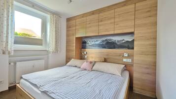 A bedroom with a wooden headboard, a bed with checkered bedding, a window with curtains, and a wall-mounted light fixture.