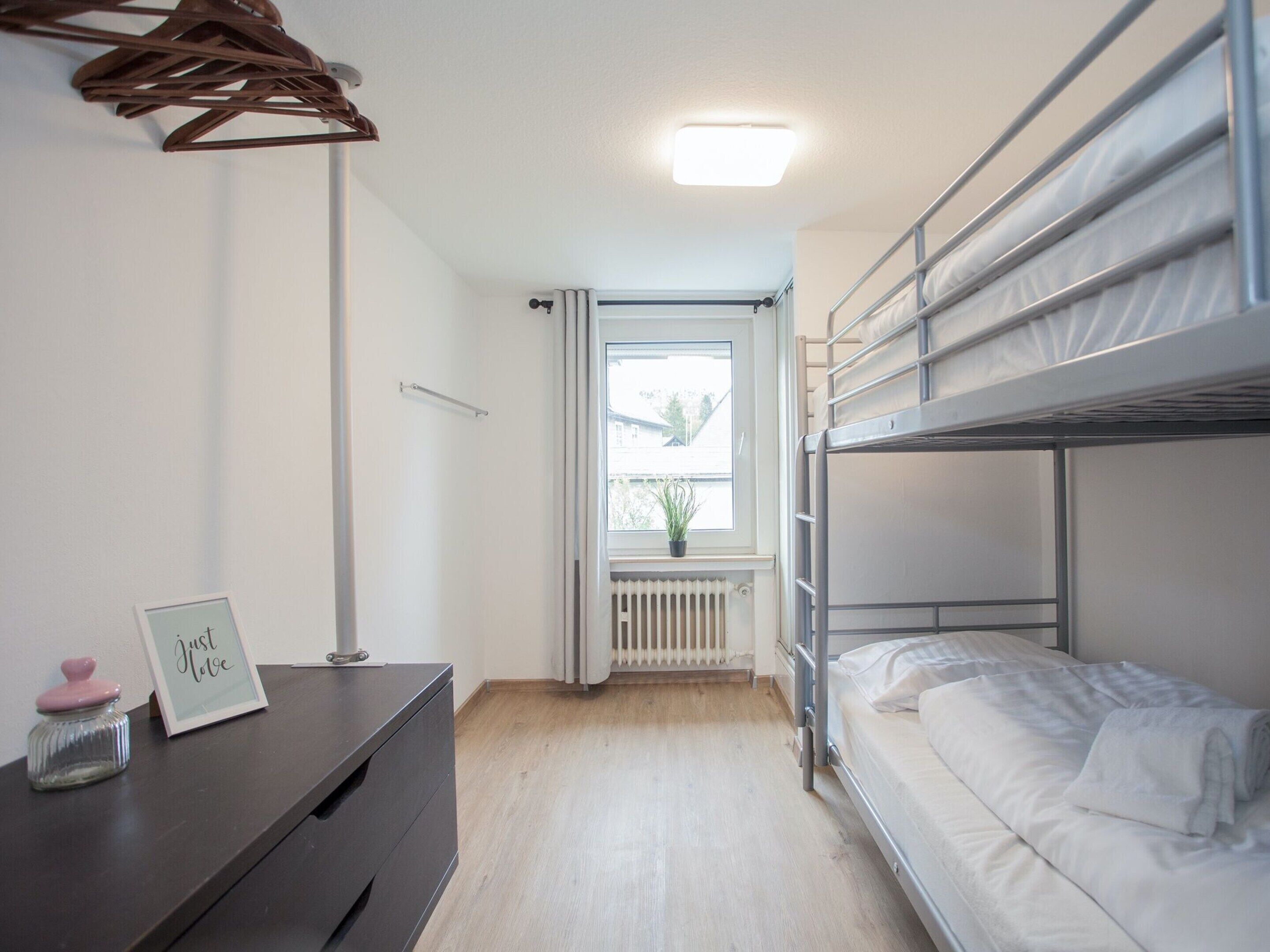 Een kleine kamer met stapelbedden, een dressoir, een radiator en een raam met uitzicht.