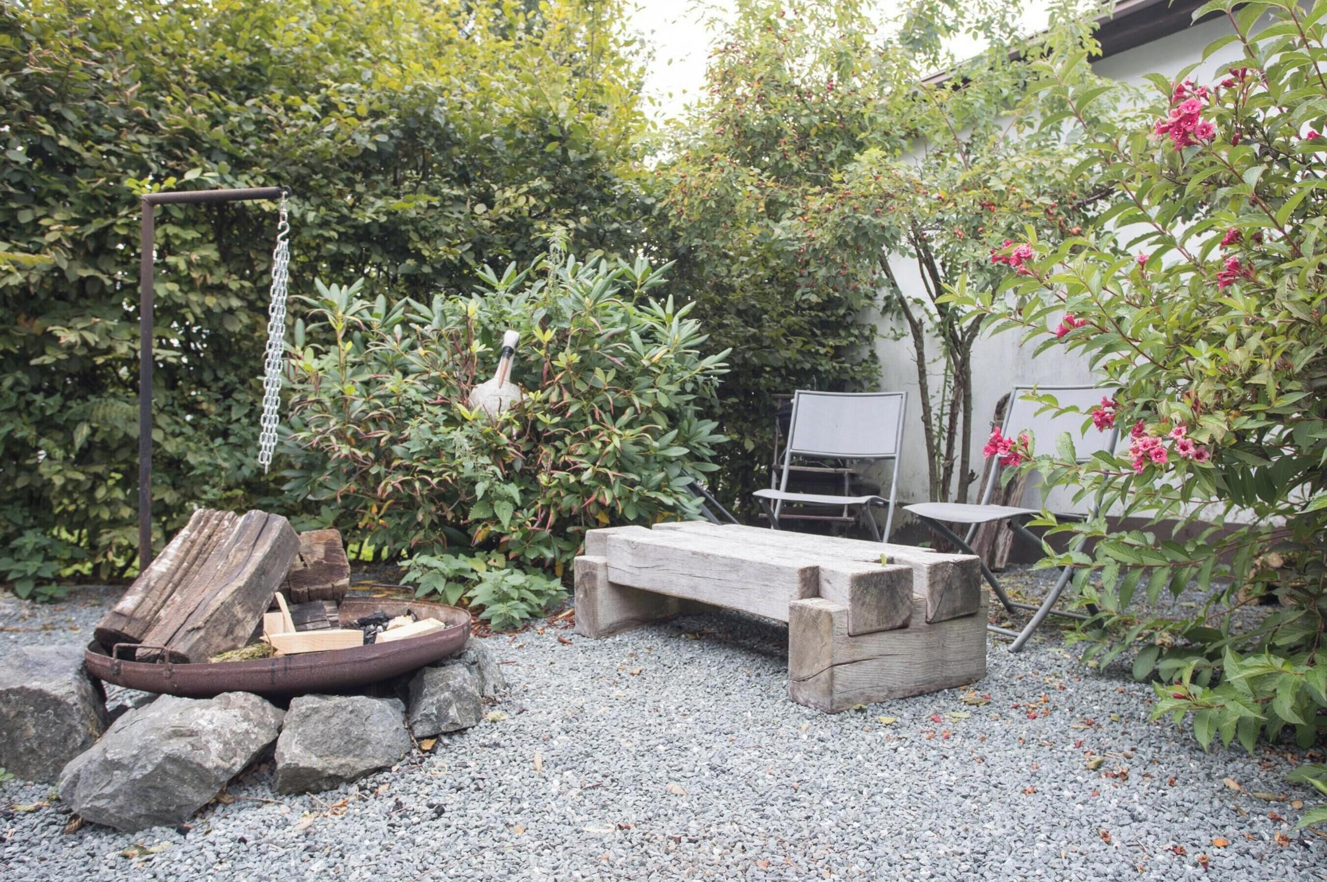 A garden with a fire pit, wooden bench, and a metal chair.