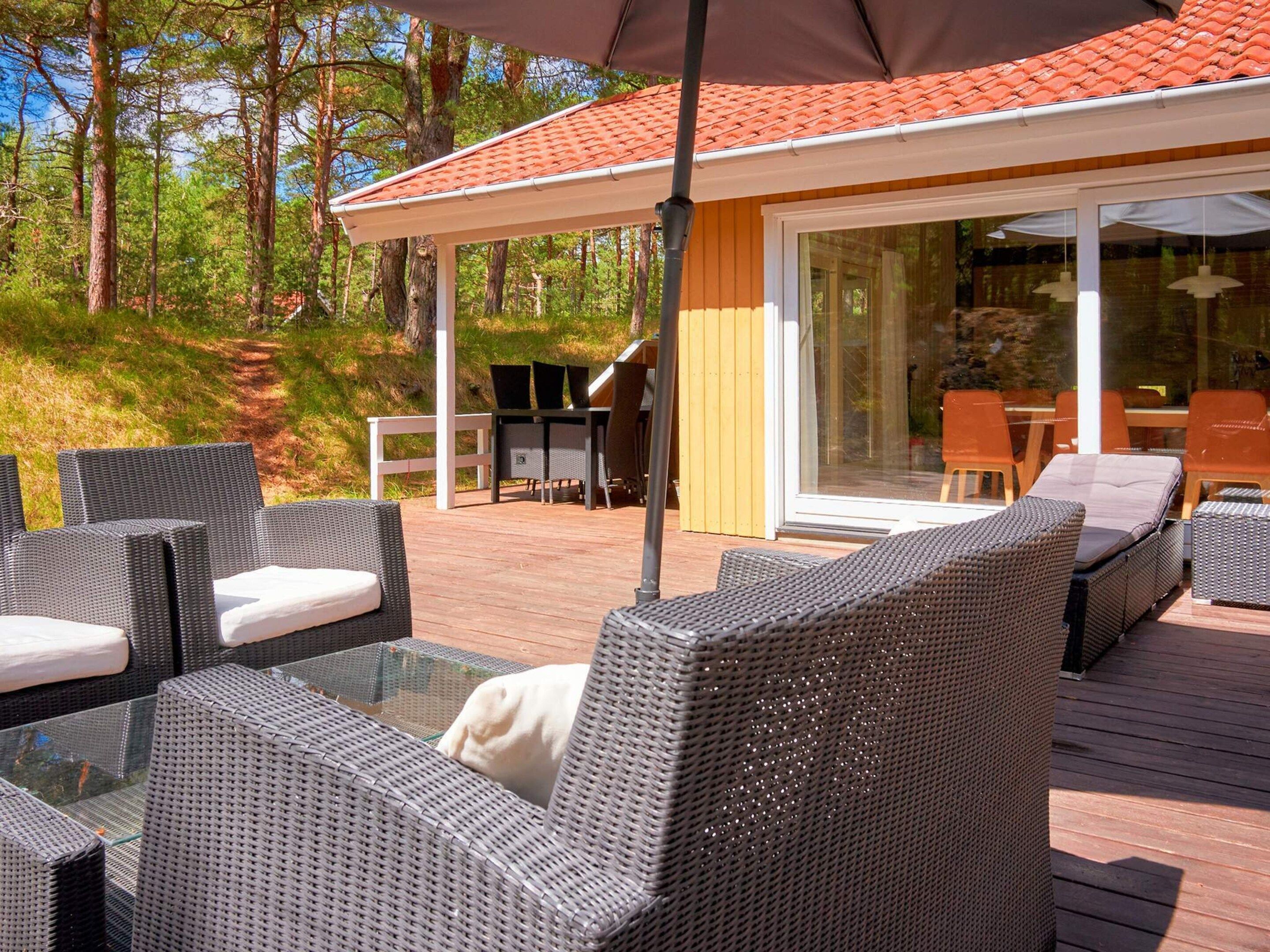 Une terrasse extérieure avec des meubles en osier, un espace couvert et une porte vitrée donnant sur un espace intérieur.